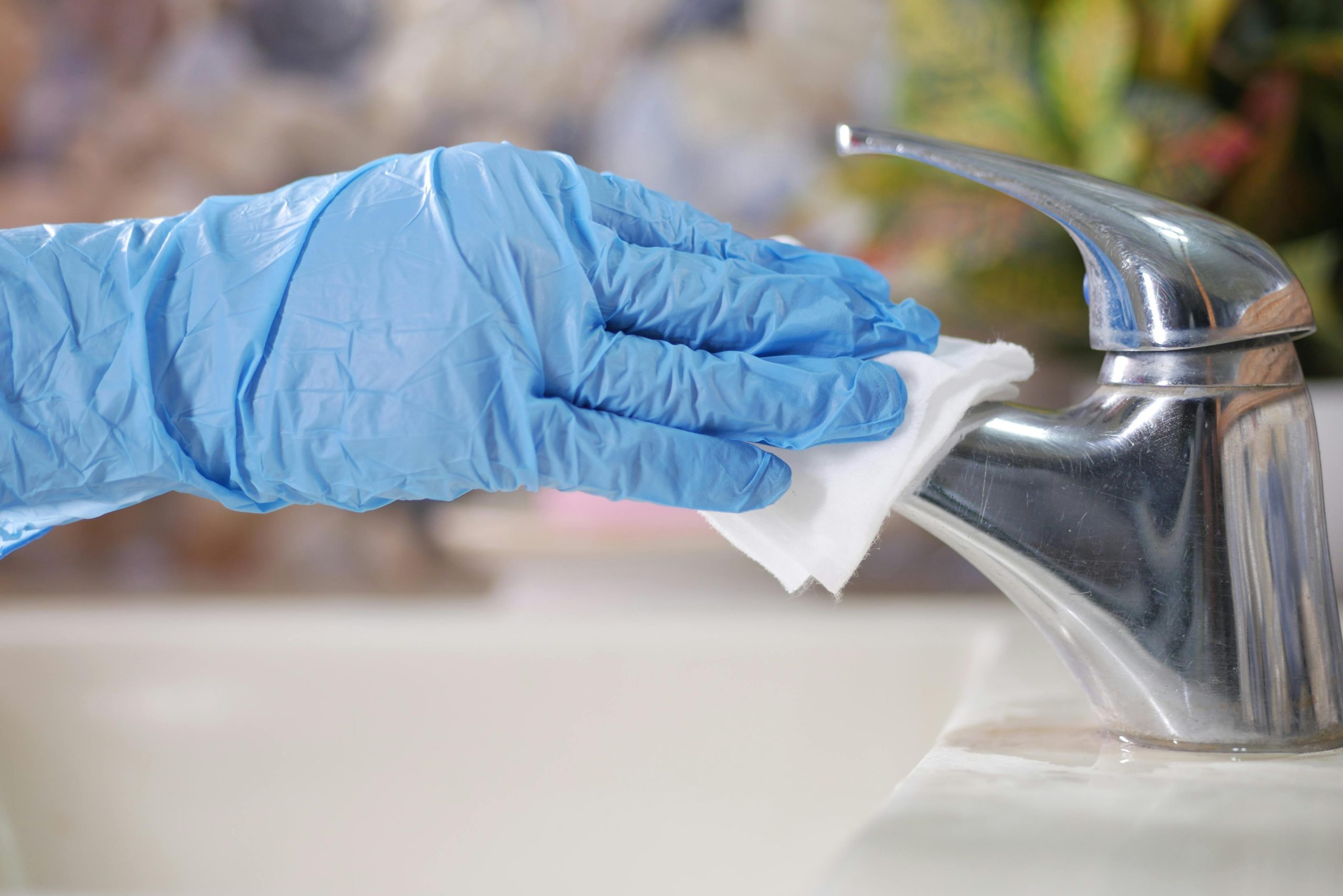 Close-up of gloved hand wiping a stainless steel faucet with a cloth indoors.